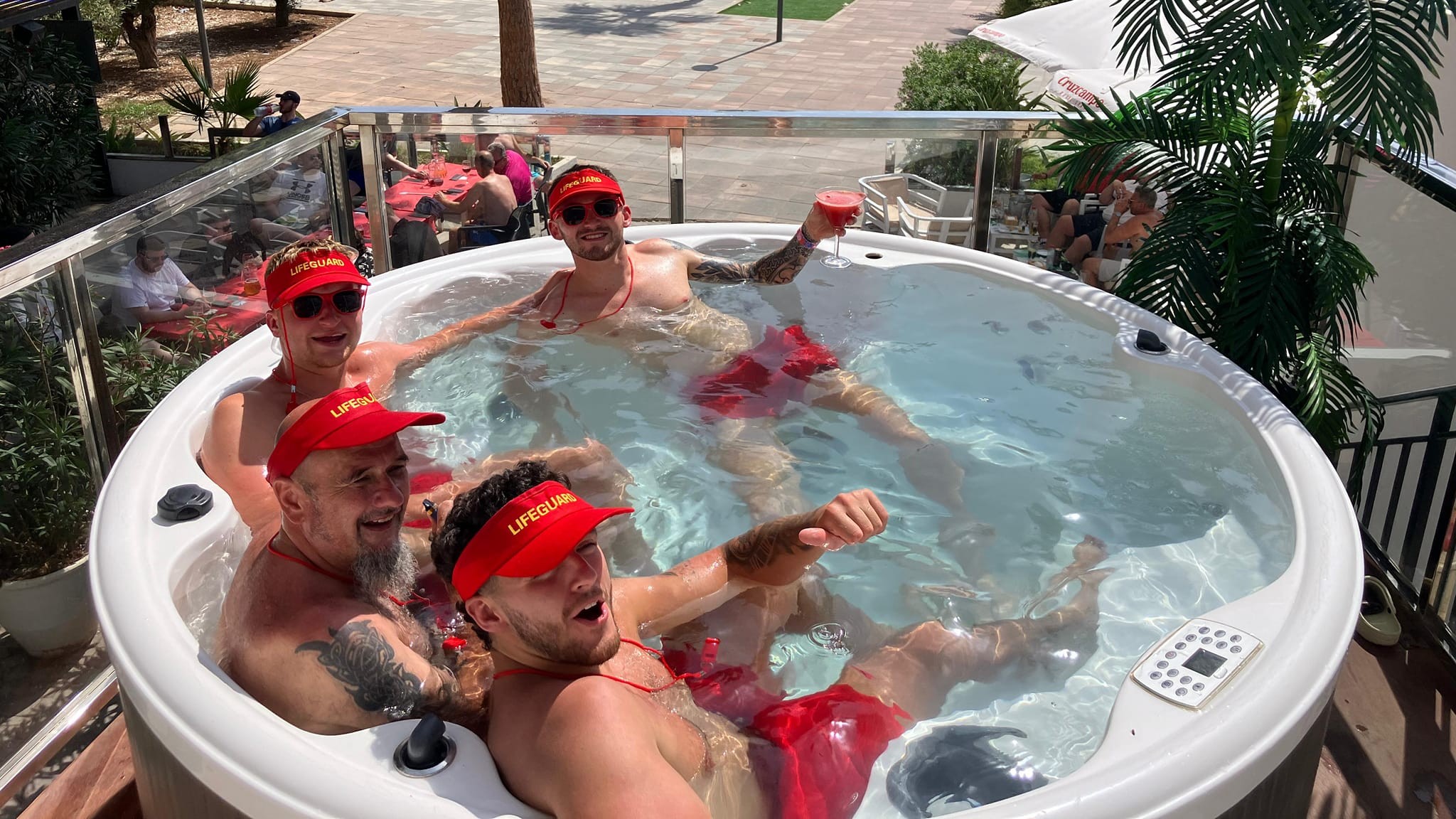 four guys with lifeguard caps on in a jacuzzi
